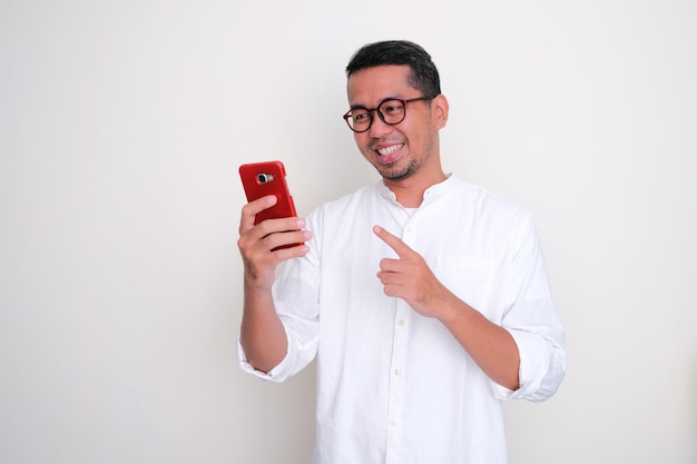 Homem asiático adulto sorrindo ao olhar para o celular e apontar para ele