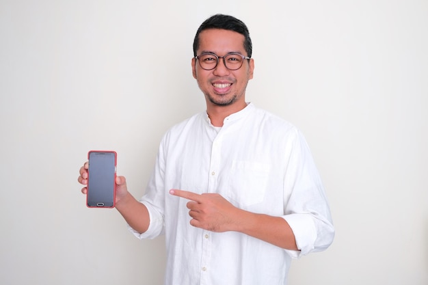 Homem asiático adulto sorrindo confiante ao apontar para a tela vazia do celular que ele segura