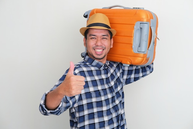 Homem asiático adulto sorrindo e levantando o polegar enquanto carregava uma bagagem de viagem