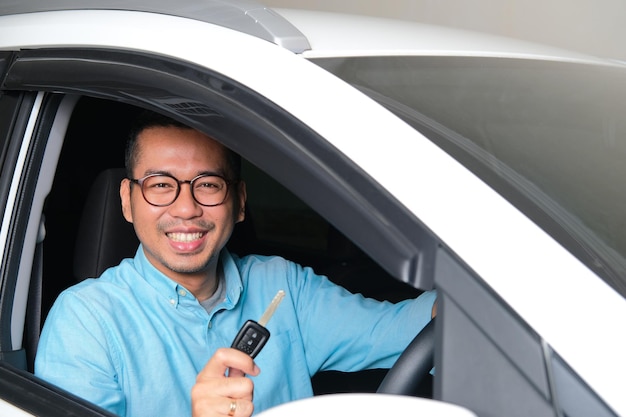 Homem asiático adulto sorrindo feliz depois de comprar um carro novo e mostrar a chave