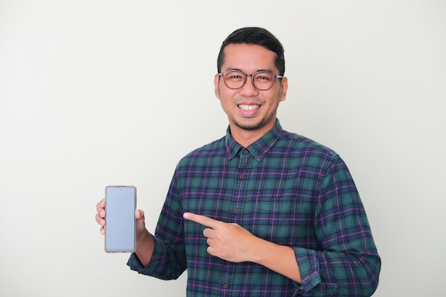 Homem asiático adulto sorrindo feliz enquanto mostra a tela do celular e aponta para ela