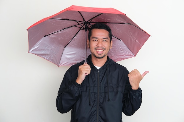 Homem asiático adulto vestindo jaqueta e usando um guarda-chuva com expressão feliz