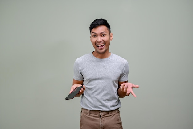 Homem asiático animado segurando seu telefone e abrindo a palma da mão contra um fundo isolado