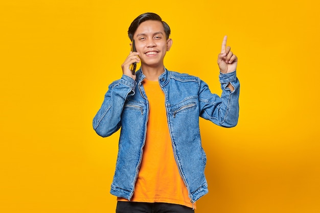 Homem asiático atraente vestindo roupas casuais, sorrindo, olhando para a câmera e apontando o dedo para cima