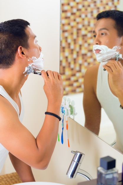 Foto homem asiático barbear na frente do espelho