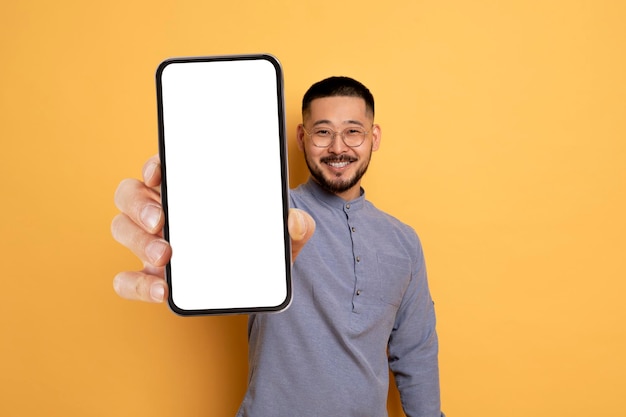 Homem asiático bonito demonstrando um grande smartphone em branco em sua mão