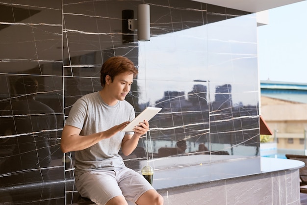 Homem asiático bonito relaxando na piscina e lendo e-book