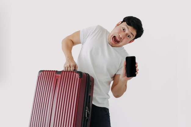 Homem asiático carregando uma mala e segurando um telefone celular mostrando aplicativo para viagens e reservas