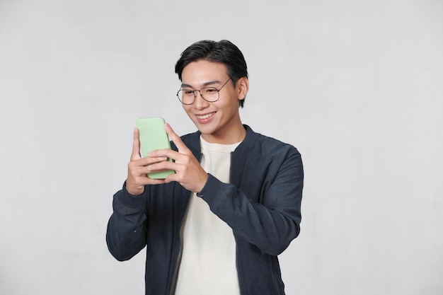 Homem asiático casual inteligente usando smartphone no fundo do estúdio