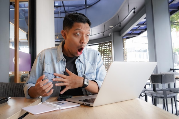 Homem asiático chocado cara wow surpreso usando laptop e telefone celular em café compras on-line
