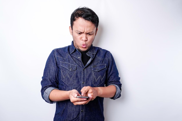 Homem asiático chocado vestindo camisa azul e segurando seu telefone isolado por fundo branco