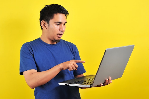 Homem asiático chocou com o que viu no laptop, isolado em um fundo amarelo