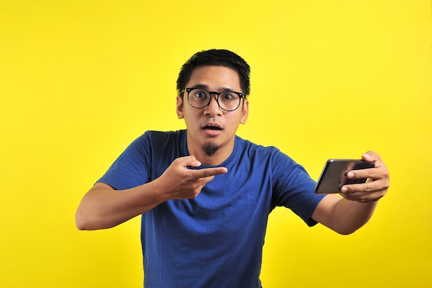 Homem asiático chocou com o que viu no smartphone, isolado em fundo amarelo