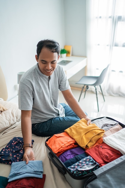 Homem asiático, colocando suas roupas na mala