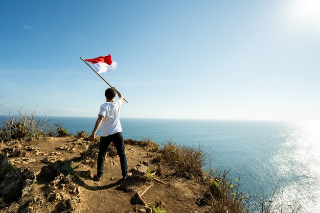 Homem asiático com bandeira da indonésia no topo da montanha