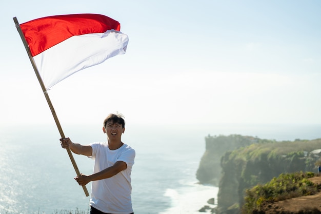 Foto homem asiático com bandeira da indonésia no topo da montanha