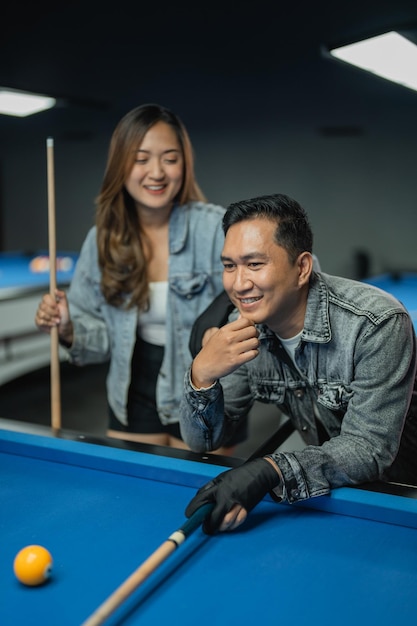 Foto homem asiático com jaqueta jeans jogando bilhar com seu amigo no estúdio de bilhar