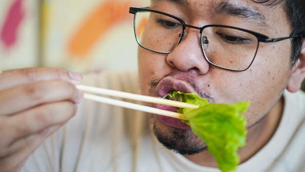 Homem asiático com óculos come deliciosa alface no restaurante