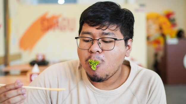 Homem asiático com óculos come delicioso sushi no restaurante