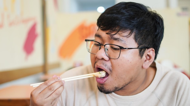 Homem asiático com óculos come delicioso sushi no restaurante