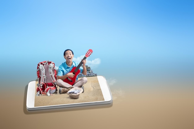 Homem asiático com um gorro e uma mochila tocando violão para ganhar dinheiro na praia