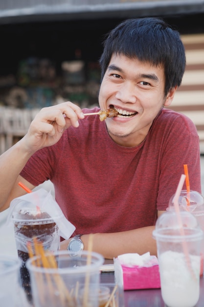 Homem asiático comendo um pedaço de carne grelhada com cara de felicidade