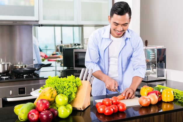 Homem asiático cortando vegetais na cozinha doméstica preparando salada