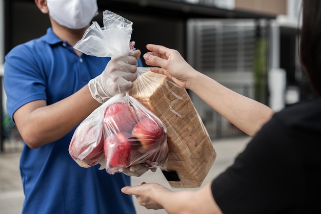 Homem asiático de entrega usa máscara protetora em uniforme azul e pronto para enviar saco de comida de entrega