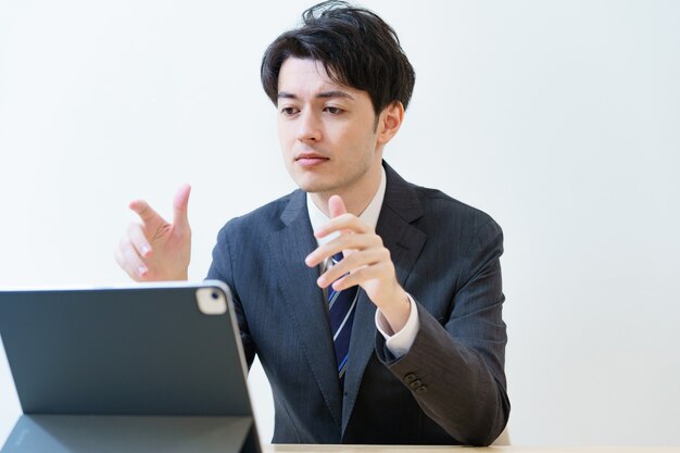 Homem asiático de terno falando para a tela de um tablet pc