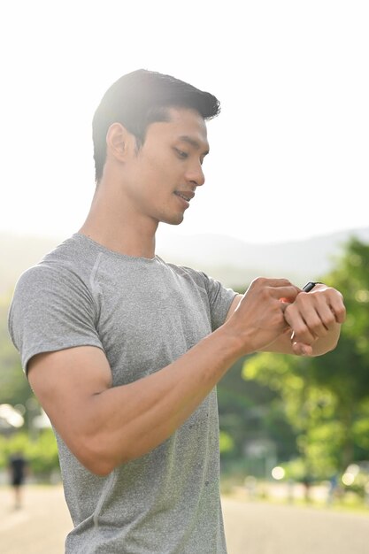 Homem asiático desportivo e bonito olhando para seu smartwatch esportivo