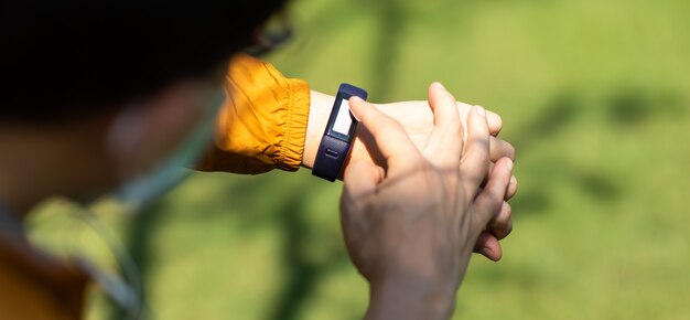 Homem asiático do esporte, verificando o desempenho ou o rastreamento do pulso de freqüência cardíaca. esporte e fitness ao ar livre. corredor masculino procurando relógio inteligente de esportes. usar máscara cirúrgica durante o surto de coronavírus e gripe