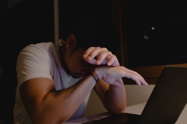 Homem asiático dorme no laptop enquanto trabalhava até tarde da noite.