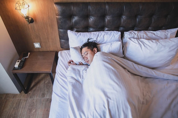 Homem asiático dormindo fortemente na cama branca