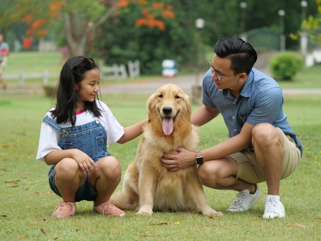 Homem asiático e menina com cachorro golden retriever no parque