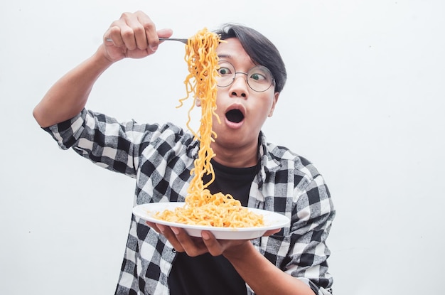 Homem asiático em camisa casual come macarrão instantâneo usando garfo com fome