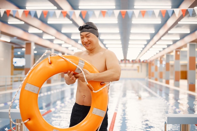 Homem asiático em pé na piscina interna e segurando um círculo de natação