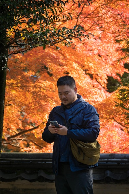 Homem asiático enquanto usa telefone celular sob Folhas de árvore de bordo durante o outono com mudança de cor na folha em amarelo laranja e vermelho