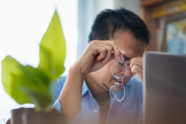 Homem asiático estressado enquanto trabalhava no laptop em casa Trabalhando em conceitos domésticos