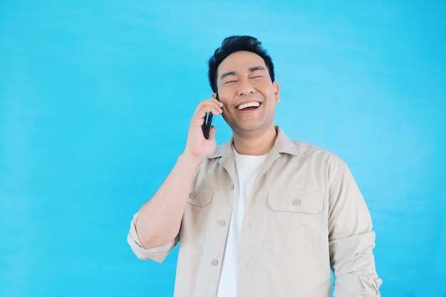 Homem asiático falando ao telefone em pé sobre fundo azul