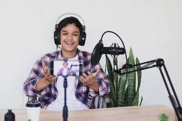 Homem asiático faz um vlog usando smartphone e microfone, explicação de gestos e expressão alegre