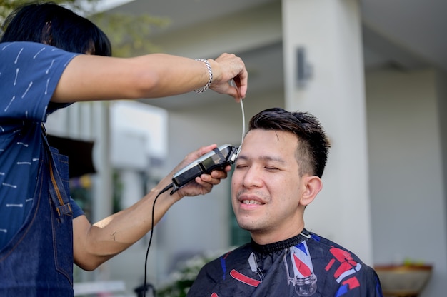 Homem asiático fazendo corte de cabelo e negócios de salão de beleza em casa. Barbearia ao ar livre no jardim. Distanciamento social e novo estilo de vida normal.