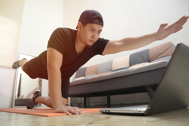 Foto homem asiático fazendo exercícios em casa enquanto assiste a instruções de vídeo on-line laptop exercícios em casa