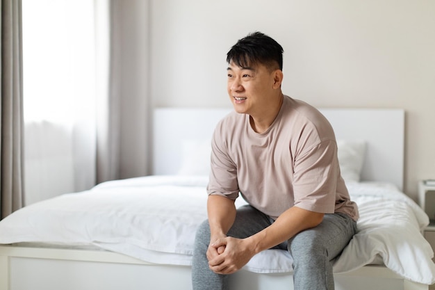 Homem asiático feliz desfrutando de manhã feliz sentado na cama