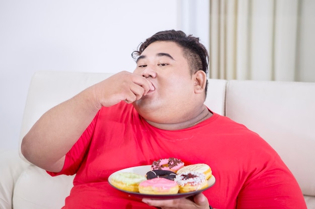 Homem asiático gordo mordendo um donut em sua casa