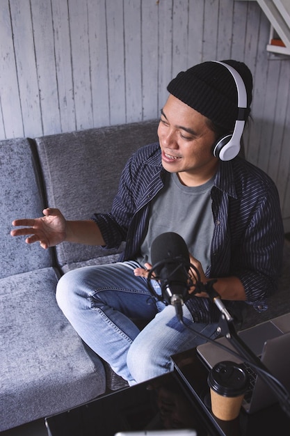 Homem asiático gravando um podcast com fone de ouvido e microfone. Podcaster fazendo podcasts de áudio em casa