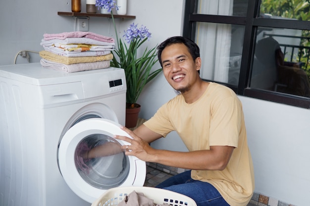 Homem asiático lavando roupa em casa carregando roupas na máquina de lavar