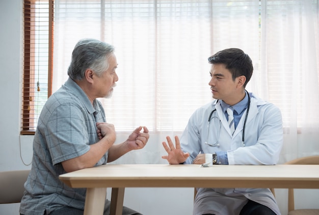 Homem asiático mais velho sênior perguntando jovem médico caucasiano sobre indicações e contra-indicações da nova medicina, cuidados de saúde e medicina conceito com espaço de cópia.