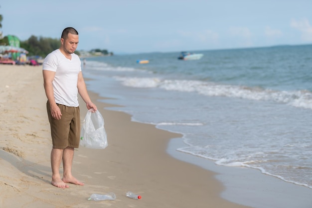 Homem asiático mantém lixo no interior do mar, voluntários da praia, mantendo garrafa de plástico de lixo