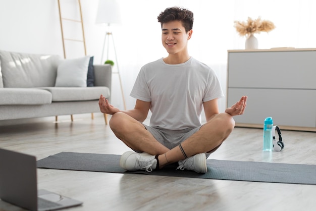 Homem asiático meditando em posição de lótus na esteira com pc