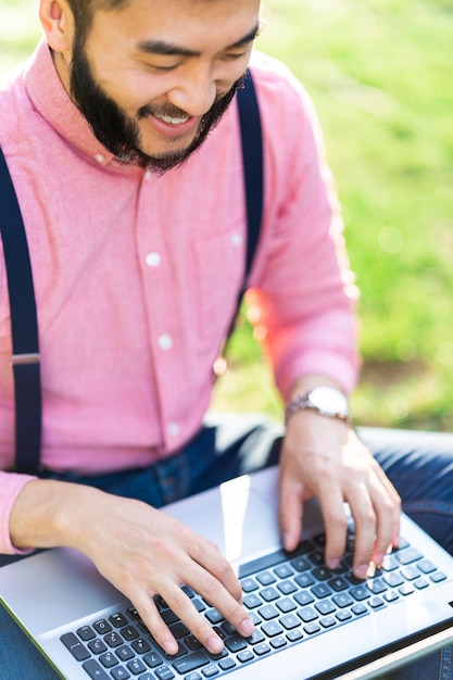 Homem asiático moderno trabalhando com um laptop em um parque
